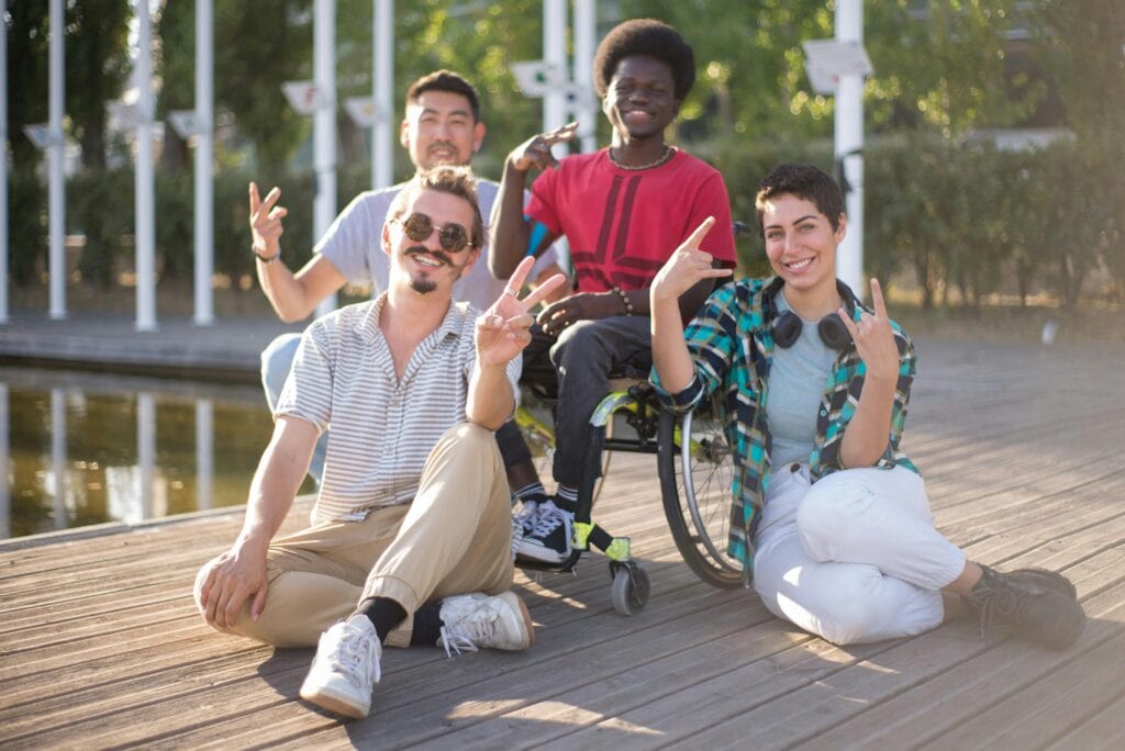 Four youth including one wheelchair user, sitting outside, smiling and posing for the camera