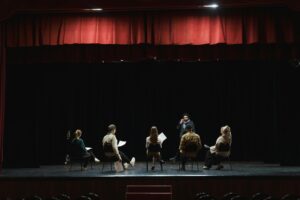 Theatre performers sitting in a circle on stage with scripts