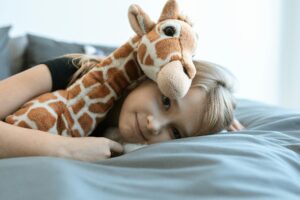 young girl lying with stuffed giraffe on her bed