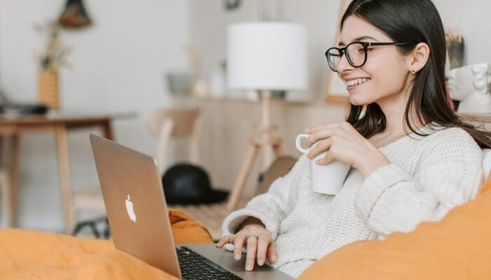 Young woman wearing glasses holding a cup of tea taking an online course on her laptop